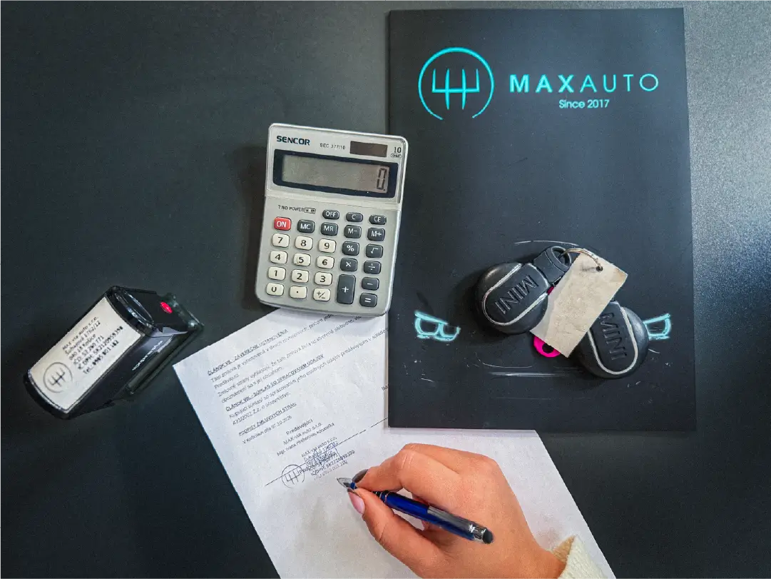 Podpisovanie zmluvy pri kalkulačke, s kľúčmi od auta a priečinkom Maxauto