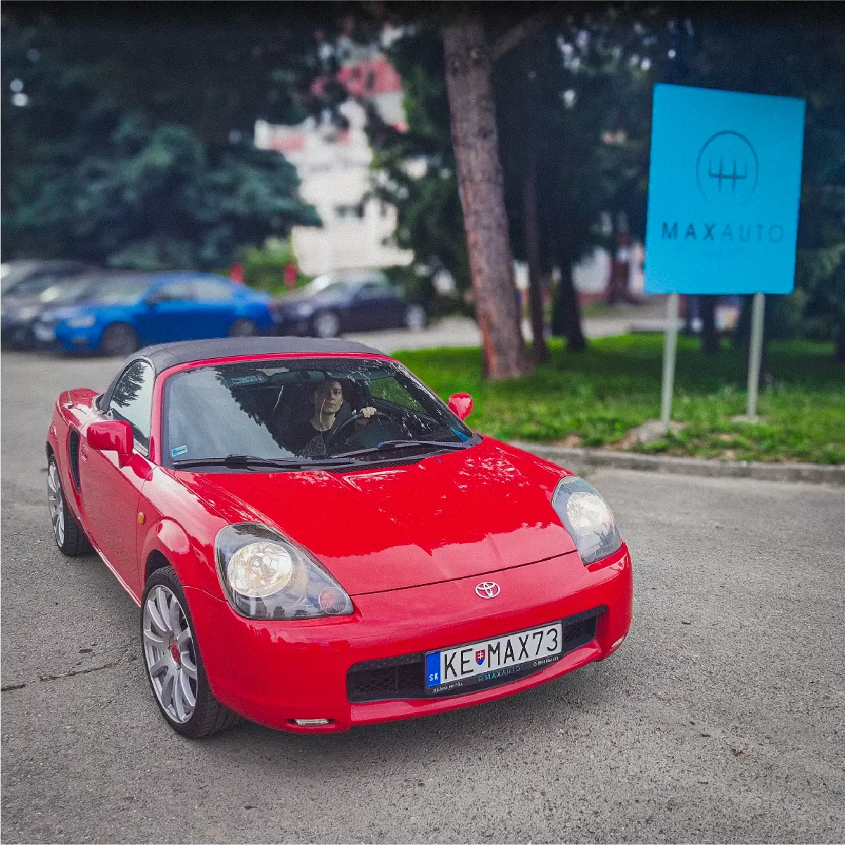 Červená Toyota pred modrou tabuľou Maxauto